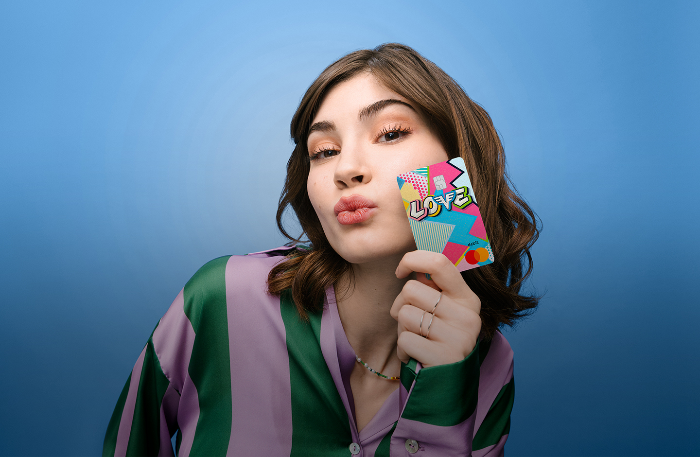 Eine junge Frau zeigt eine LOVE Debit Mastercard der Volksbank in die Kamera. Sie macht einen Kussmund.